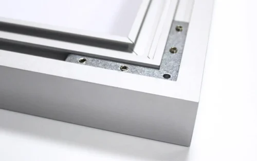 Close-up of a white metal window frame corner with screw holes and a silver gasket/weatherstrip area in the joint.