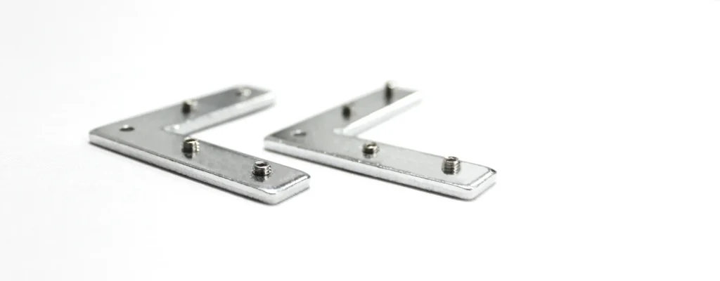 Two silver L-shaped metal brackets with small screws on a white surface