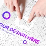 Hand placing a puzzle piece on a white jigsaw puzzle with the text 'YOUR DESIGN HERE' in purple and 'unleash your creativity'—conveying customizable design.