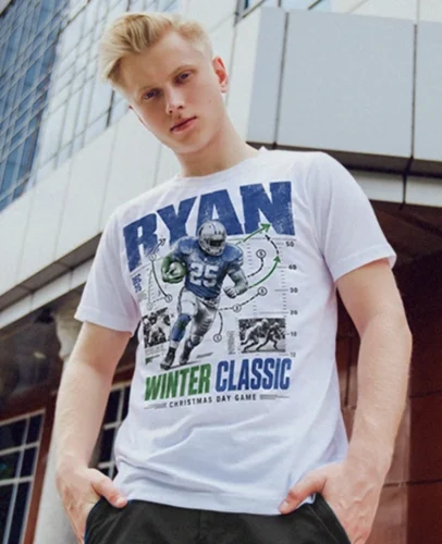 Young man wearing a white graphic T-shirt with a football player illustration and the text 'RYAN WINTER CLASSIC', standing outdoors near a modern building.